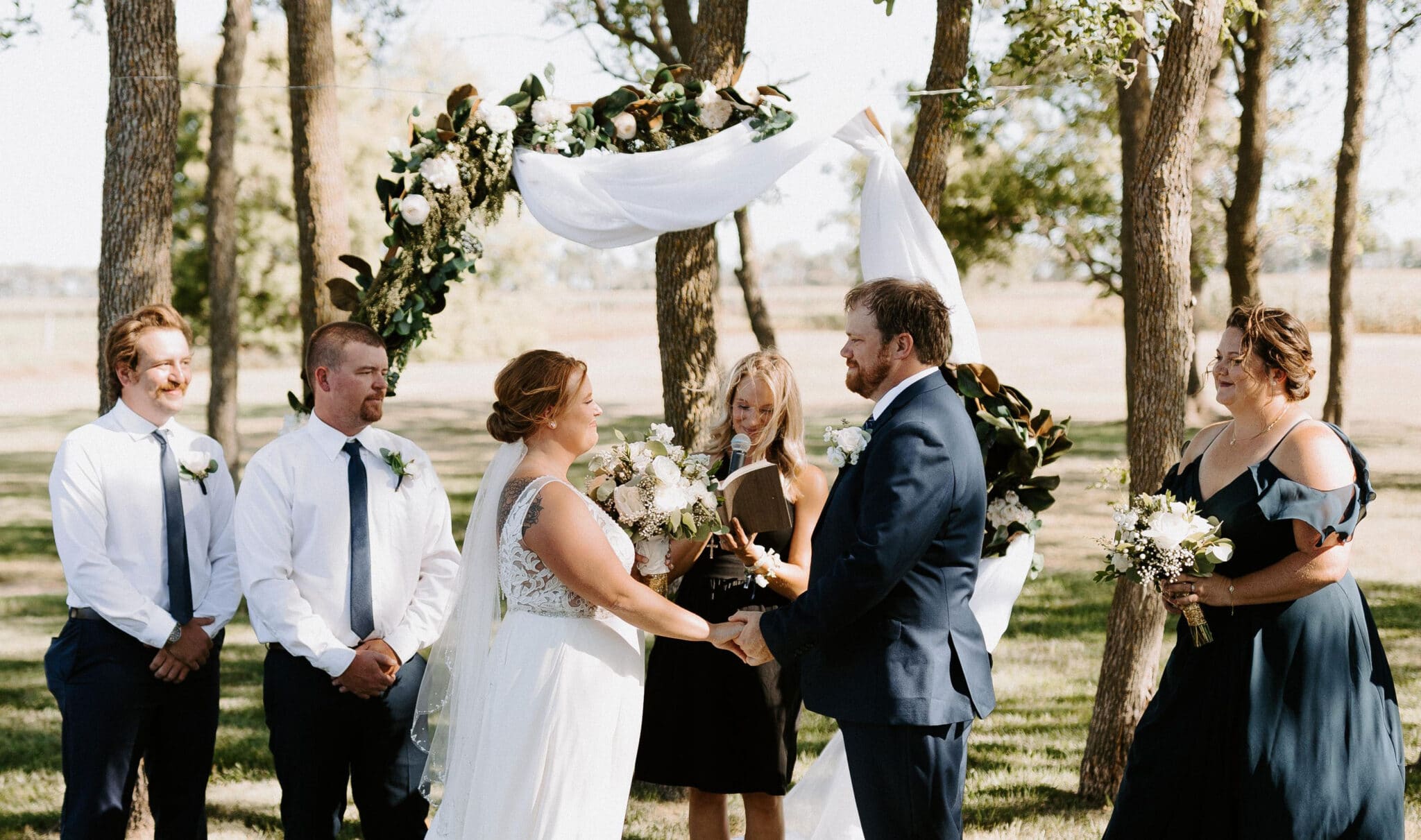 Outdoor wedding ceremony with couple exchanging vows under arch