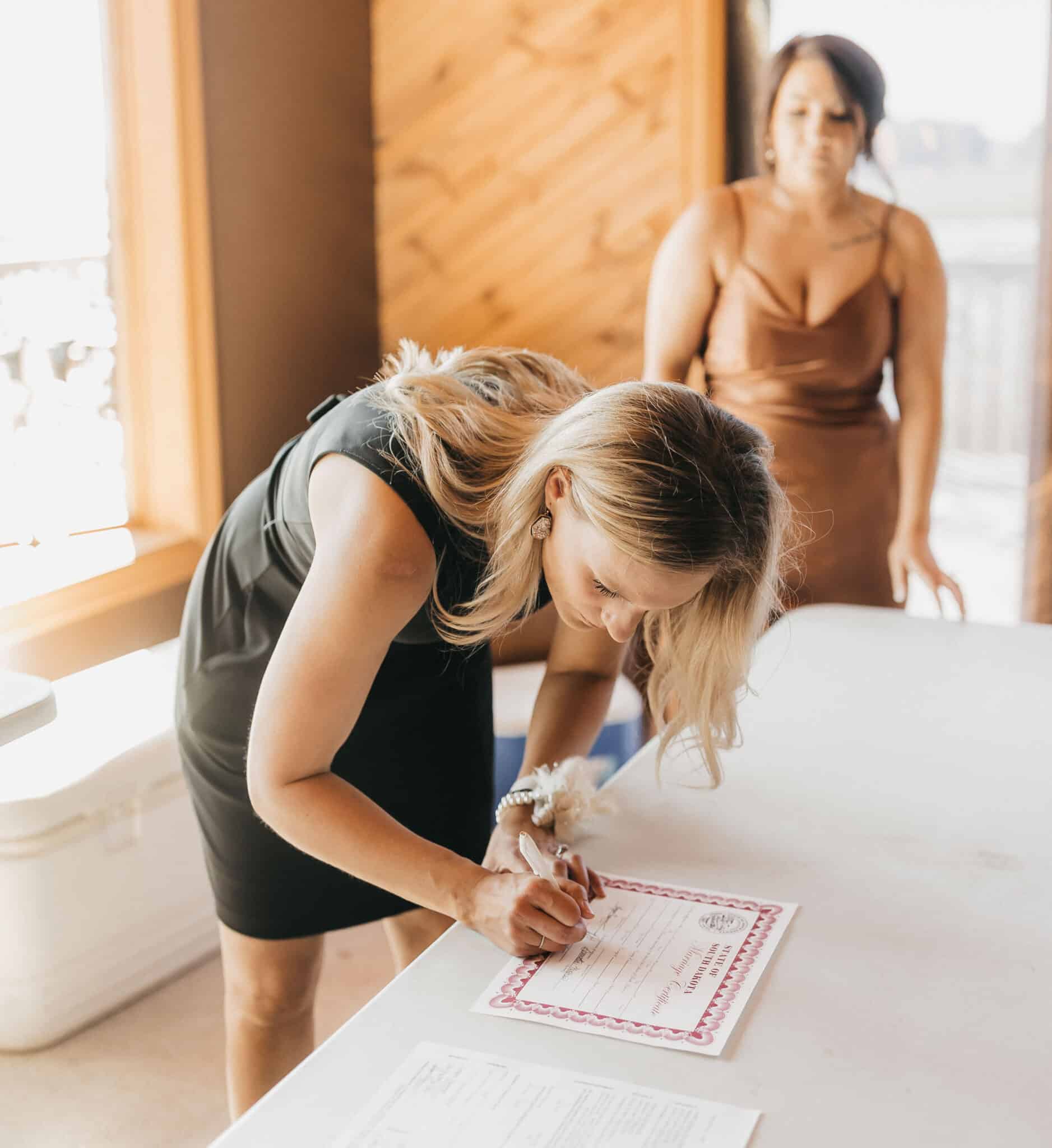 Renee Bauman signing marriage certificate at indoor ceremony table