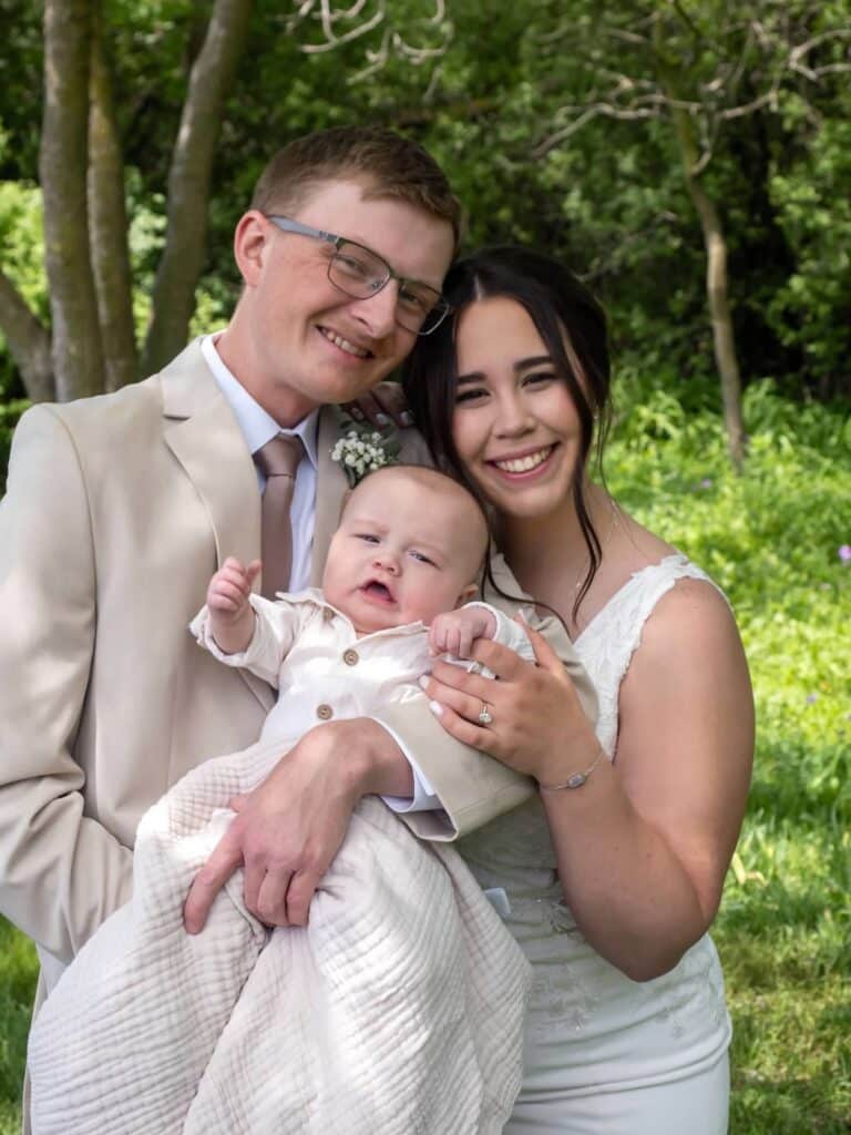 Smiling couple in wedding attire holding baby outdoors