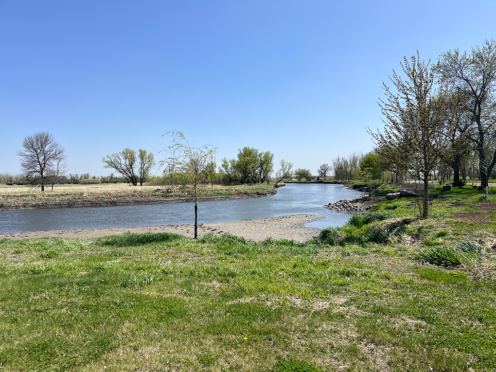 Curving river through grassy park under blue sky