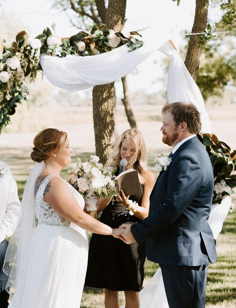 Bride and groom exchange vows beneath a floral wedding arch