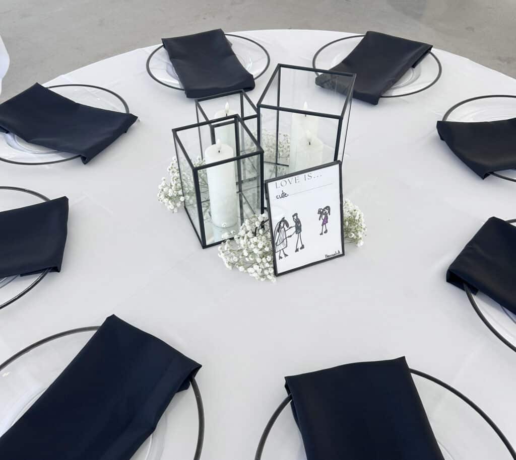 Elegant white table with black napkins, lanterns, and flowers