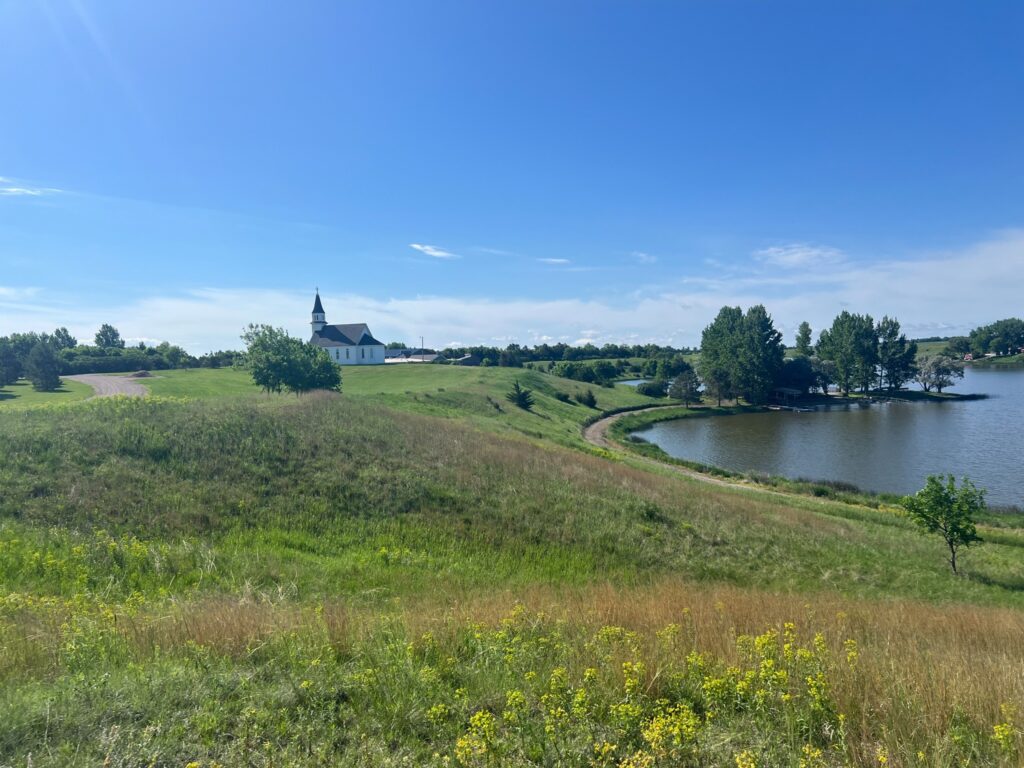 White country church overlooking a lake and green hills