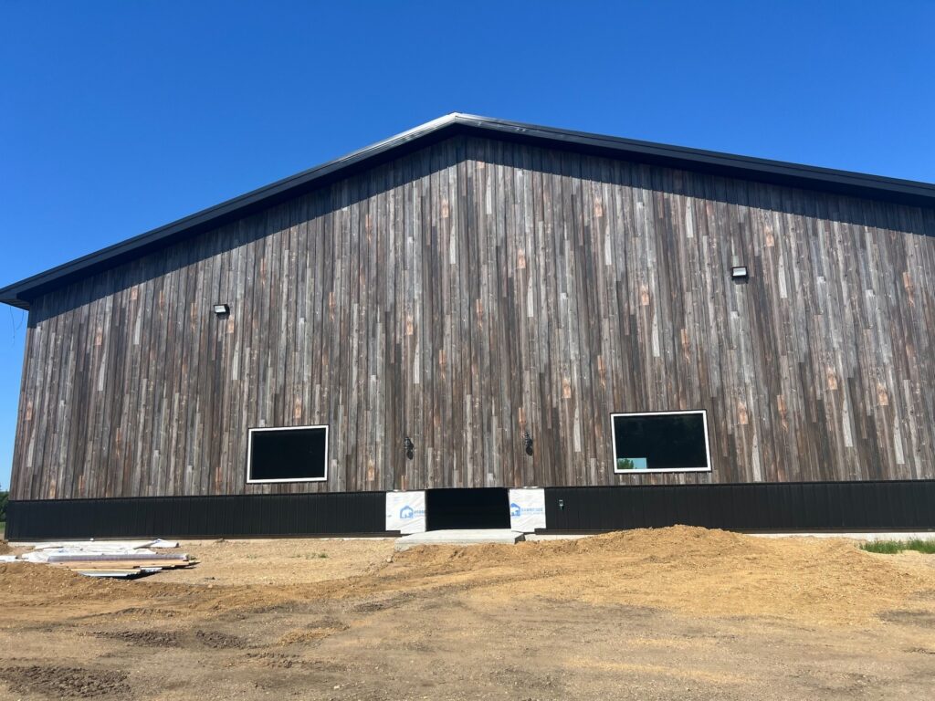 Wood-clad barn under construction beneath a clear blue sky