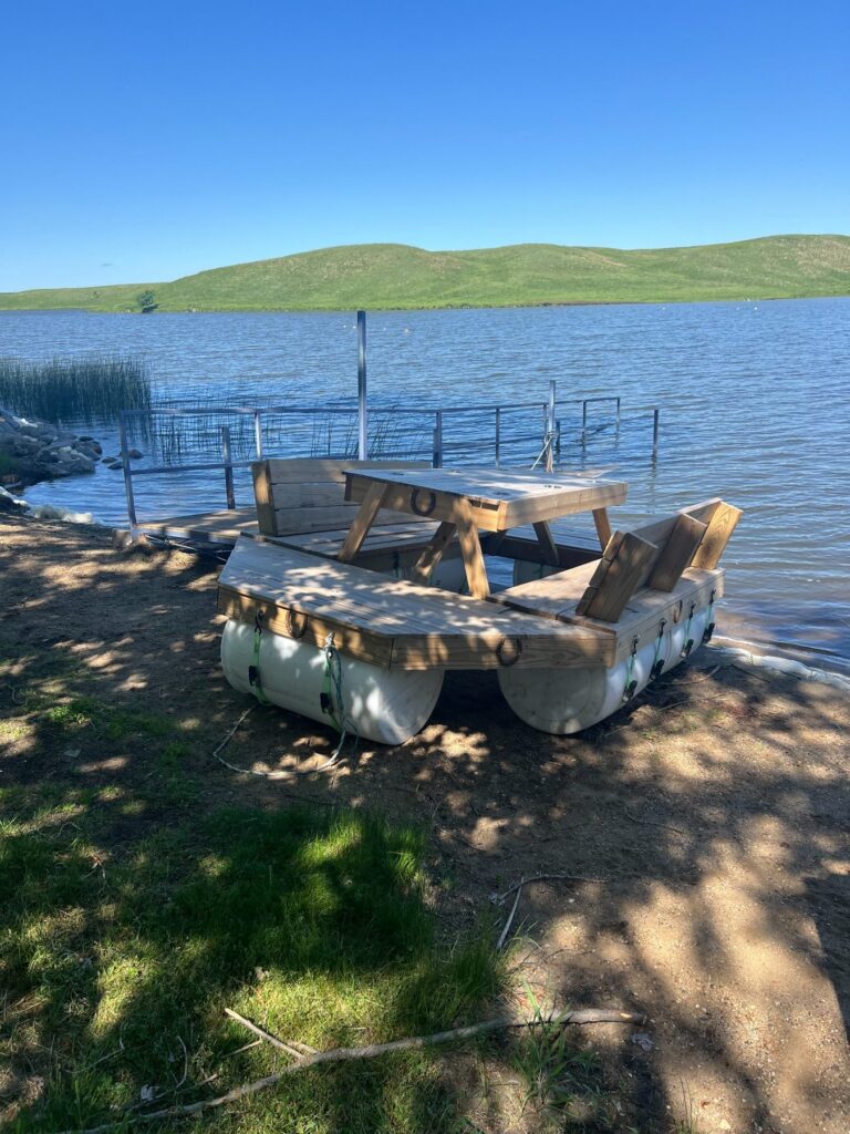 Wooden picnic raft beside lake under clear blue sky