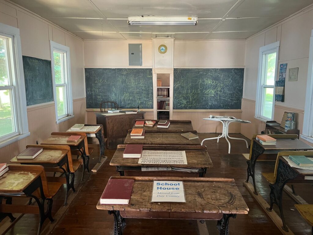 Historic classroom with wooden desks, books, and chalkboards
