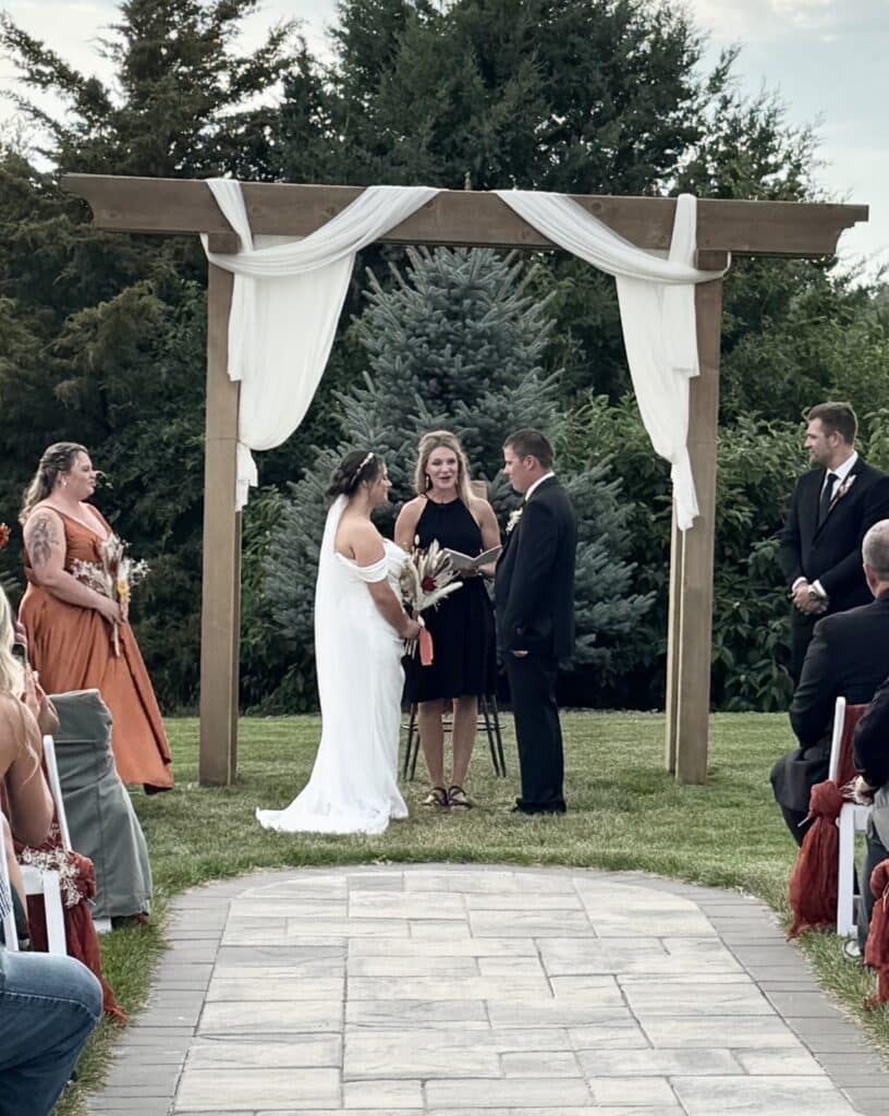 Couple exchanging vows beneath draped wooden wedding arbor