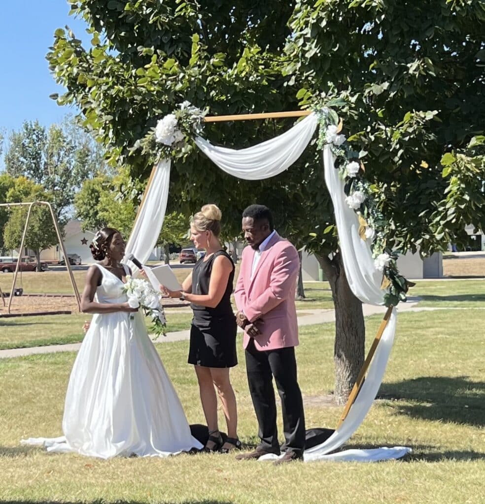 Couple exchanges vows beneath floral wedding arch outdoors