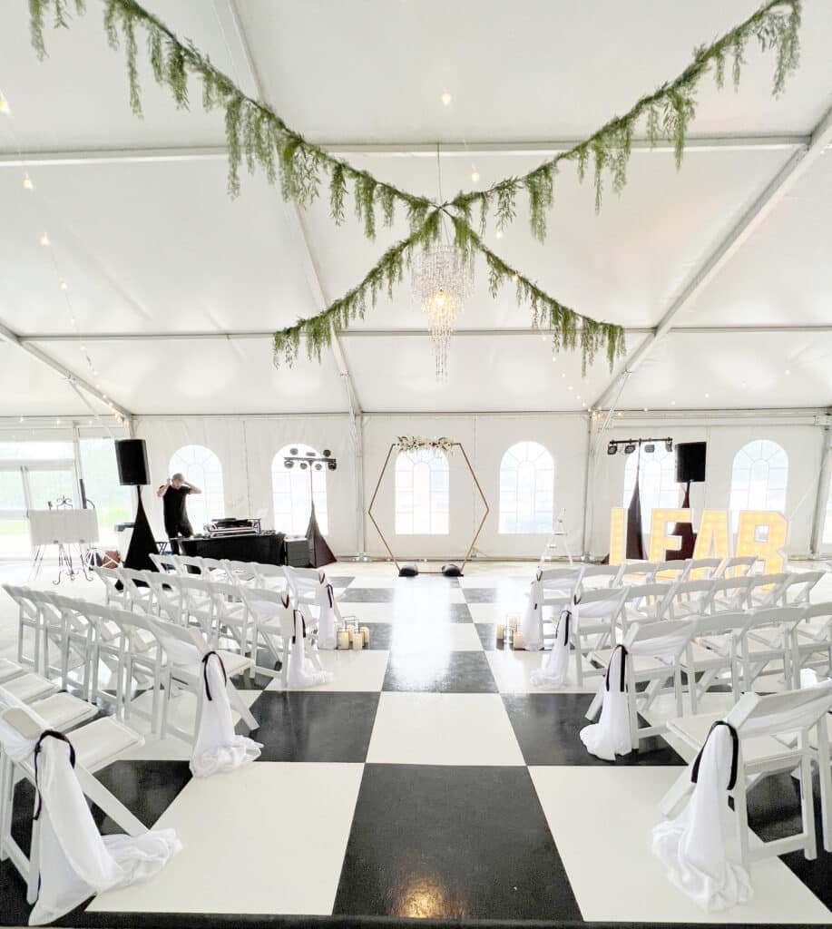 Elegant tent wedding ceremony with greenery, chandelier, and checkered dance floor