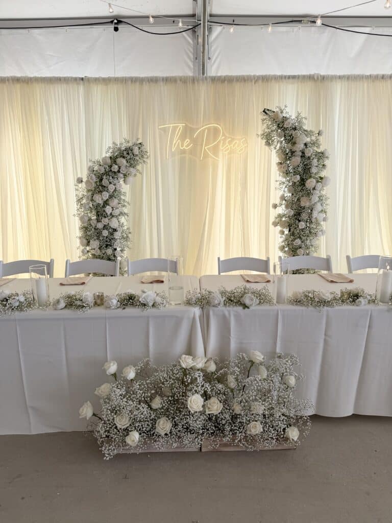 White floral wedding reception table beneath a glowing backdrop