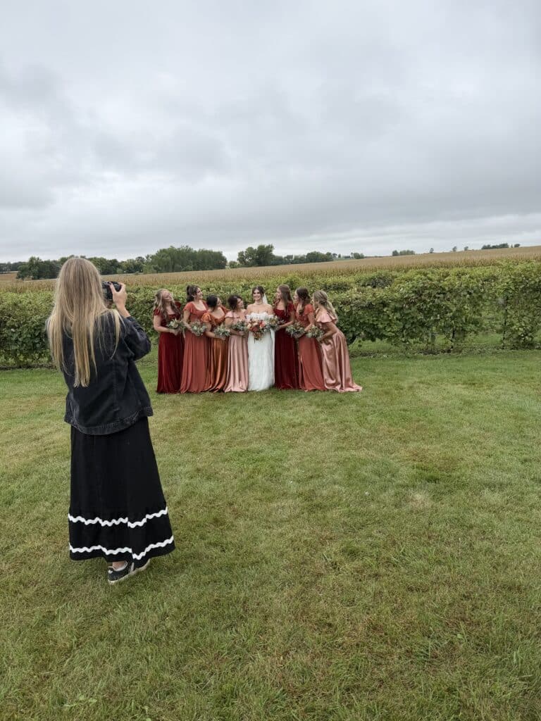 Photographer captures bridal party in vineyard beneath cloudy sky