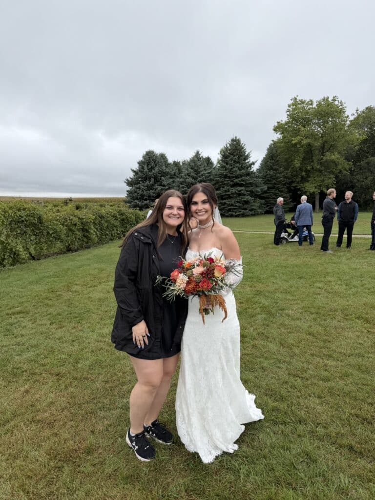 Bride and friend pose with bouquet at outdoor wedding