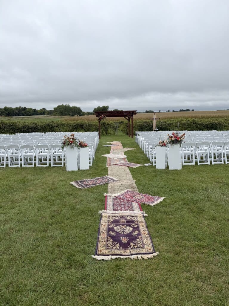 Outdoor wedding ceremony setup with chairs, rugs, and wooden arbor
