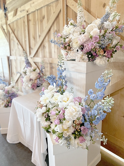 Pastel floral arrangements on white pedestals in rustic venue