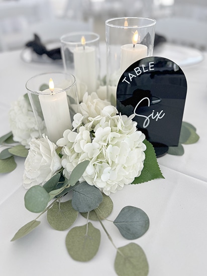 White floral centerpiece with candles and black table six sign