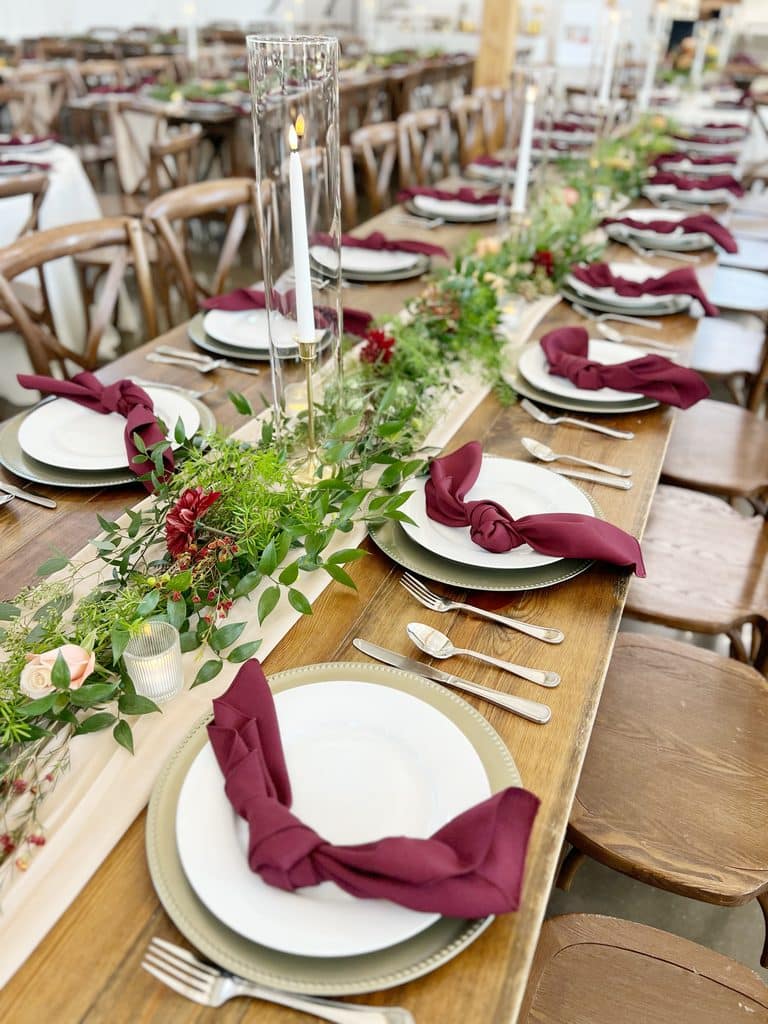 Candlelit banquet table with burgundy napkins and floral greenery