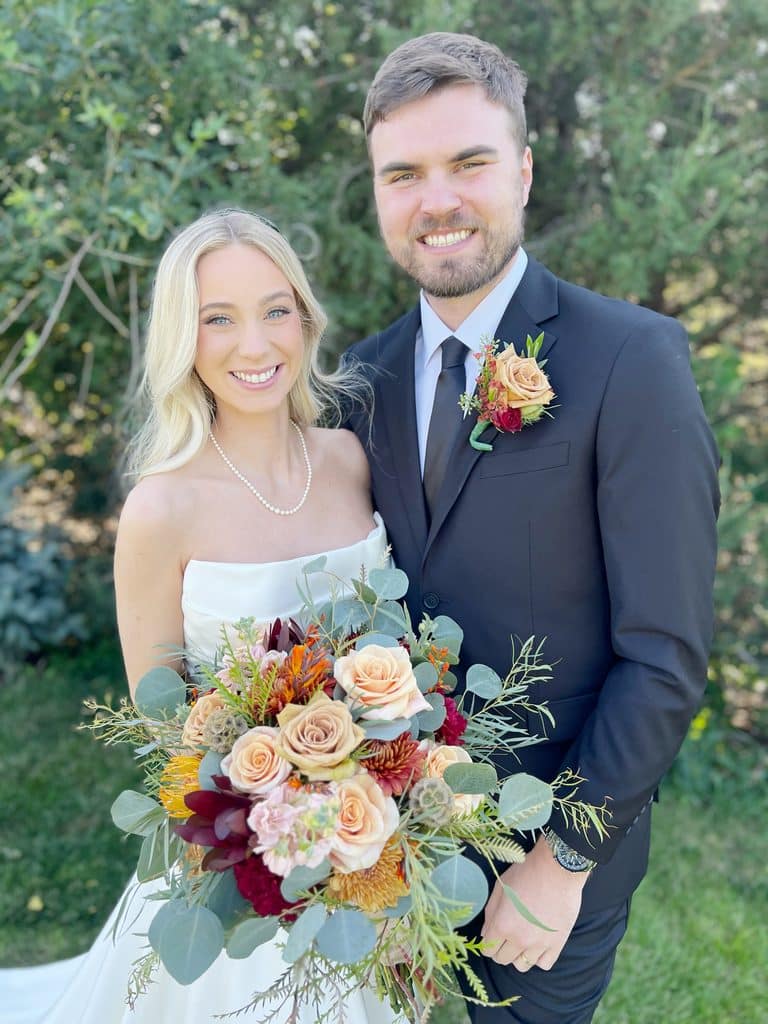 Smiling newlyweds pose outdoors with colorful wedding bouquet